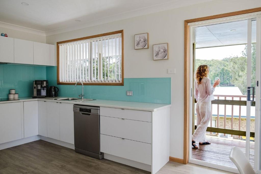 une femme debout dans une cuisine regardant par la fenêtre dans l'établissement Paradise Lake, à Yatte Yattah
