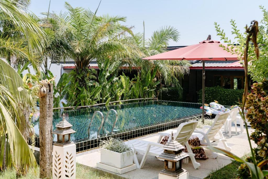 a pool with white chairs and a red umbrella at The Loft Panwa Resort in Panwa Beach