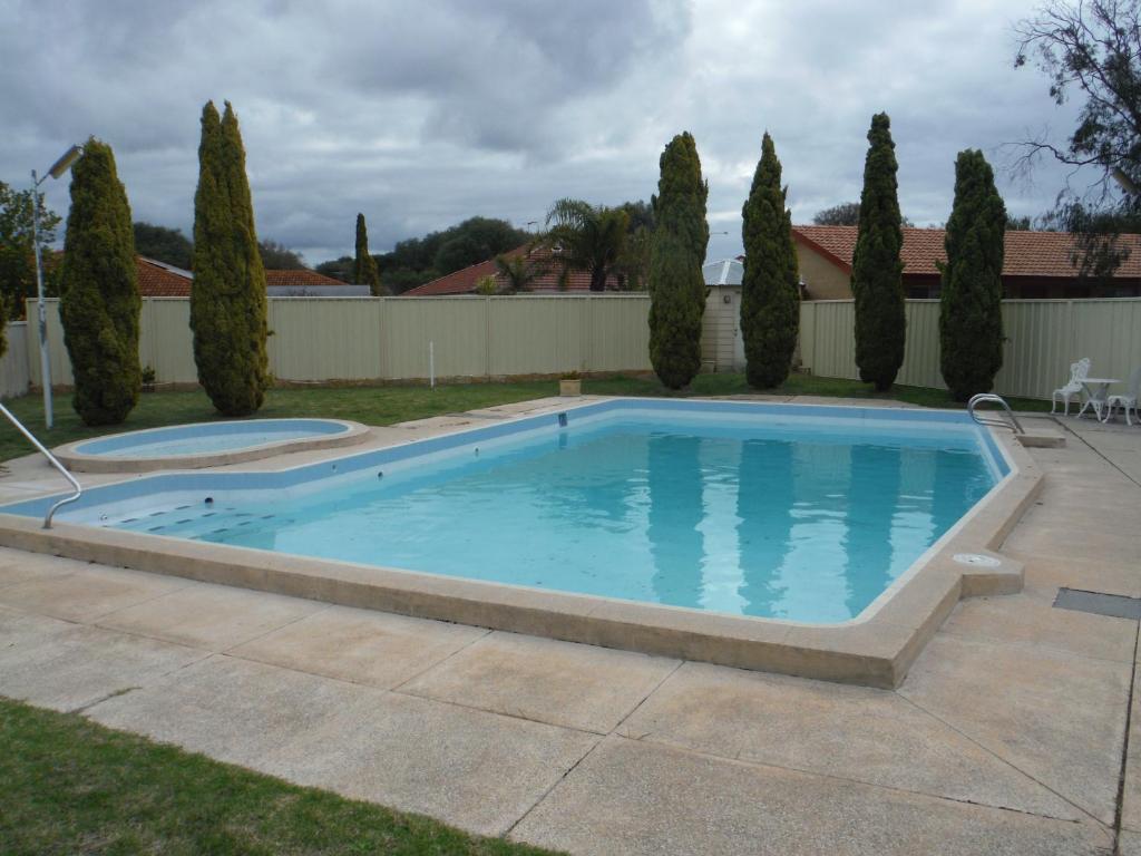 a swimming pool in a yard with trees and a fence at Restawile Motel in Busselton