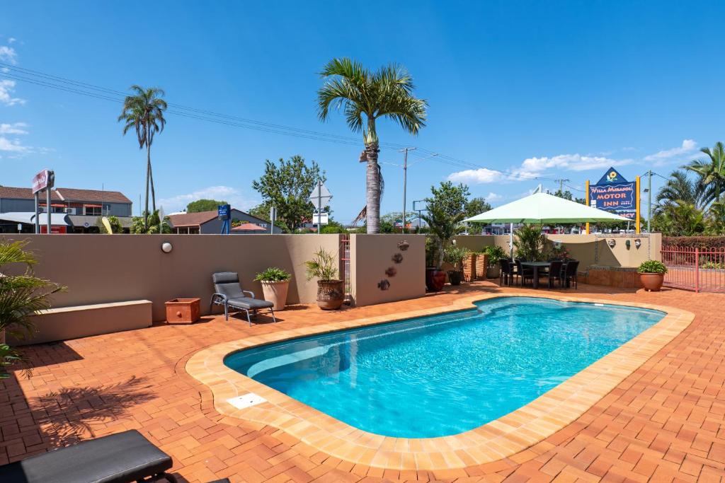 a swimming pool on a brick patio with palm trees at Villa Mirasol Motor Inn in Bundaberg