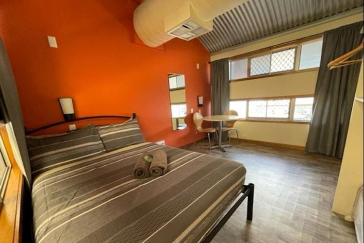 Un dormitorio con una cama grande con una pared naranja. en Red Rock Hostel, en Alice Springs