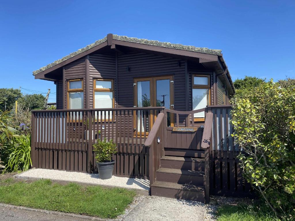 a black tiny house with a wooden railing and stairs at Lamorna in Penzance