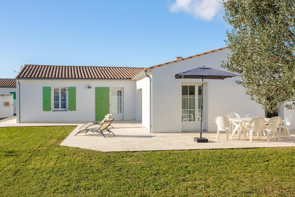 ein weißes Haus mit einem Tisch, Stühlen und einem Sonnenschirm in der Unterkunft Villa Du Chai in Sainte-Marie-de-Ré