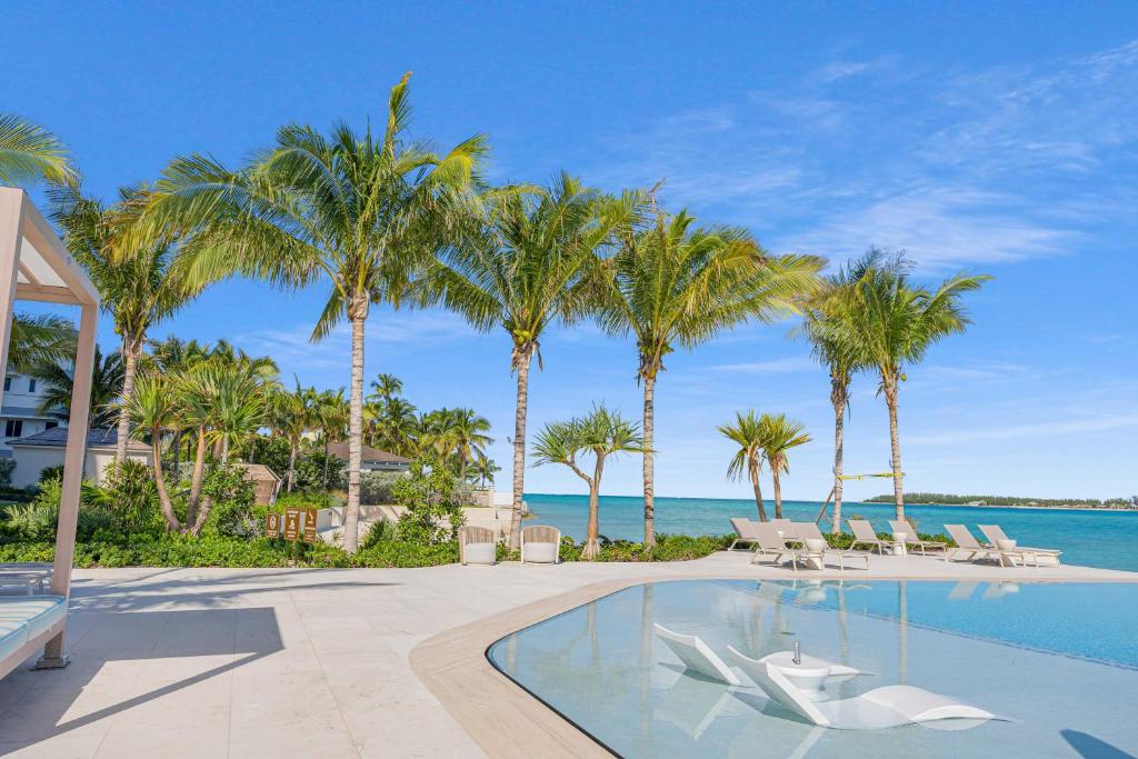 a resort swimming pool with palm trees and the ocean at Beachfront 3 bedroom Luxury Residence in Nassau