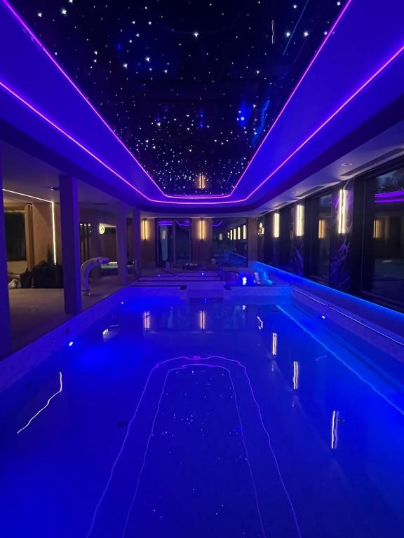 Long indoor pool under starry ceiling panels, purple LED accent lighting and reflective water surface.