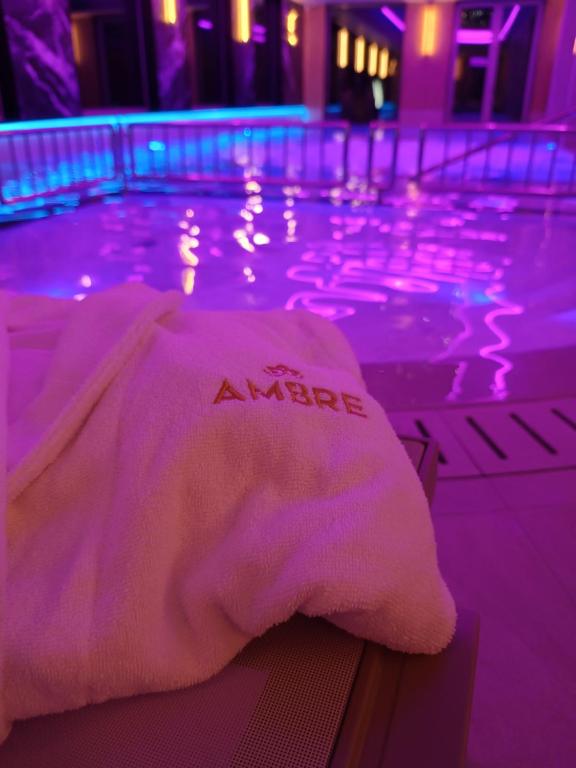 Folded Ambre-branded robe on lounger beside indoor pool, purple ambient lighting reflected in water.