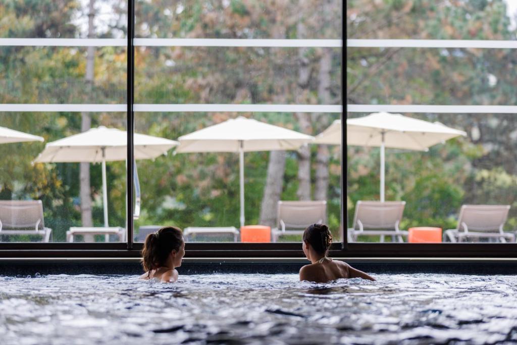 Dos niños en una piscina con sillas y sombrillas. en Mercure Aix-les-Bains Domaine de Marlioz Hôtel & Spa, en Aix-les-Bains