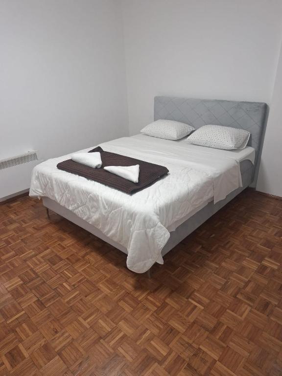 a bedroom with a bed with white sheets and a wooden floor at San centar apartment in Banja Luka