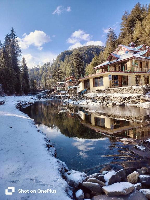 a river with snow on the ground next to houses at Shiva Valley Riverside in Jibhi