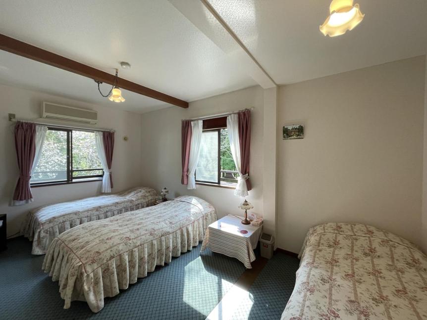 a bedroom with three beds and a table in it at ペンションあけまの森 in Daisen
