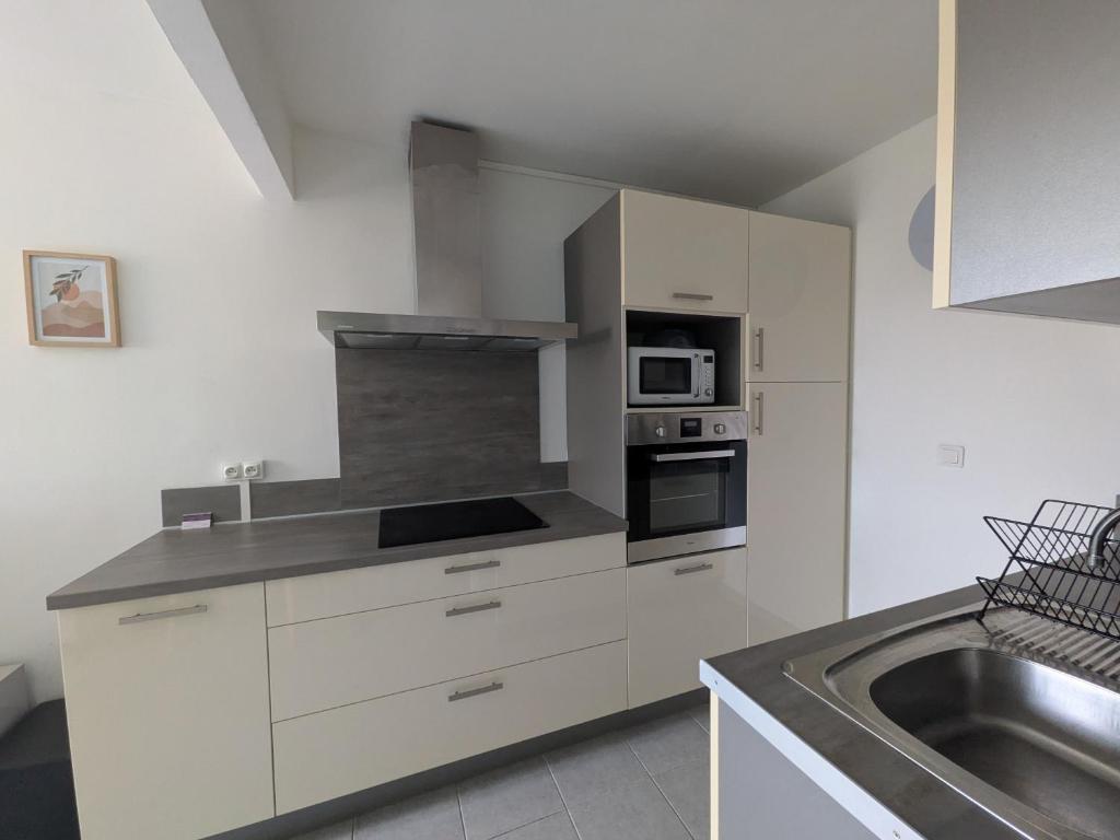 een keuken met witte kasten en een roestvrijstalen wastafel bij 150 m de la cure thermale emplacement idéal iter Cadarache in Gréoux-les-Bains