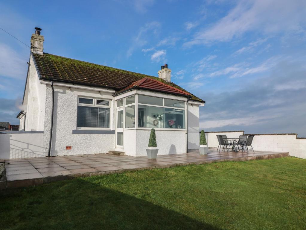 a white house with a patio with two chairs at Marchdyke Farm Cottage in Lockerbie