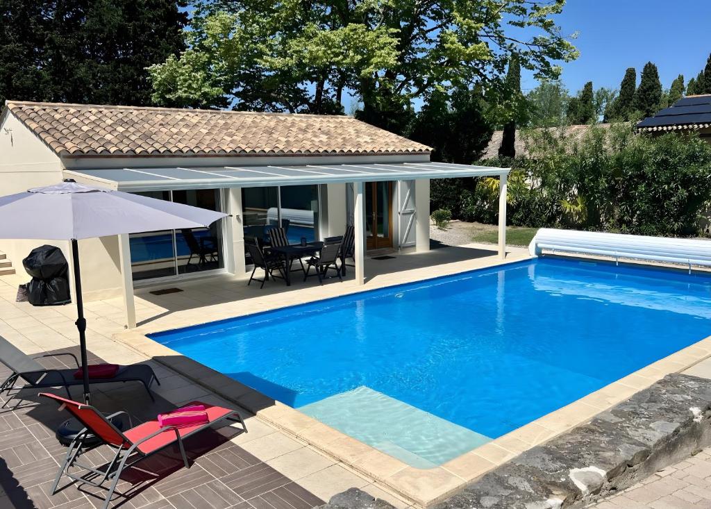 a swimming pool with two chairs and an umbrella at Gîte Tango - Les Petites Écuries in Marseillette