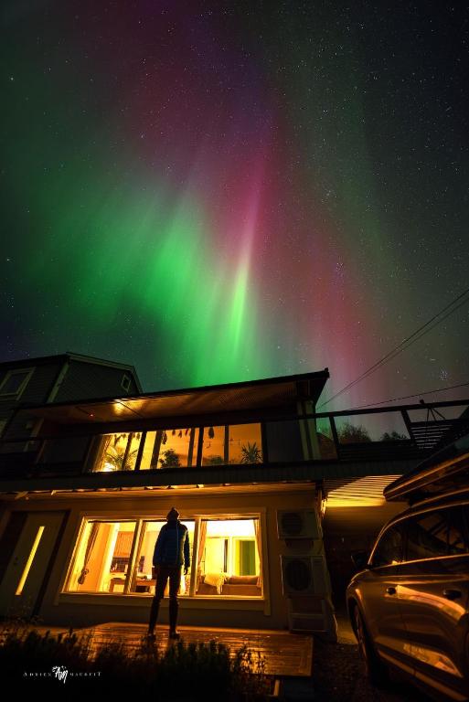a man standing in front of a house under the northern lights at Northern Lights Apartment in Mortenhals
