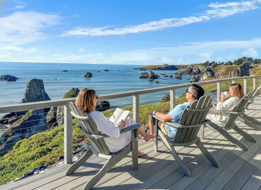 three people sitting in chairs on a deck looking at the ocean at Seaside Elegance Oceanfront Escape with 3 Suites in Carmet