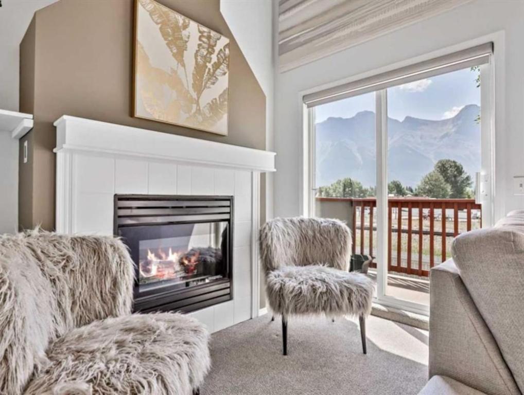 a living room with a fireplace and two chairs at Rockies 3BR Townhome w Stunning Views Near DT in Canmore