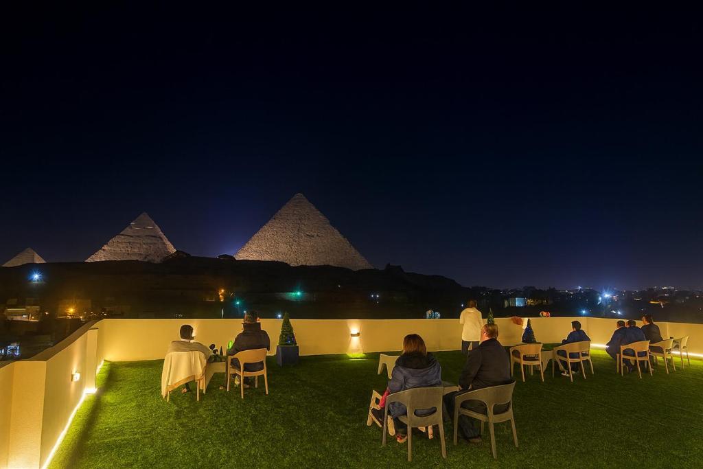 een groep mensen die 's nachts aan tafels zitten met de piramides bij The Tree Pyramids Inn in Caïro