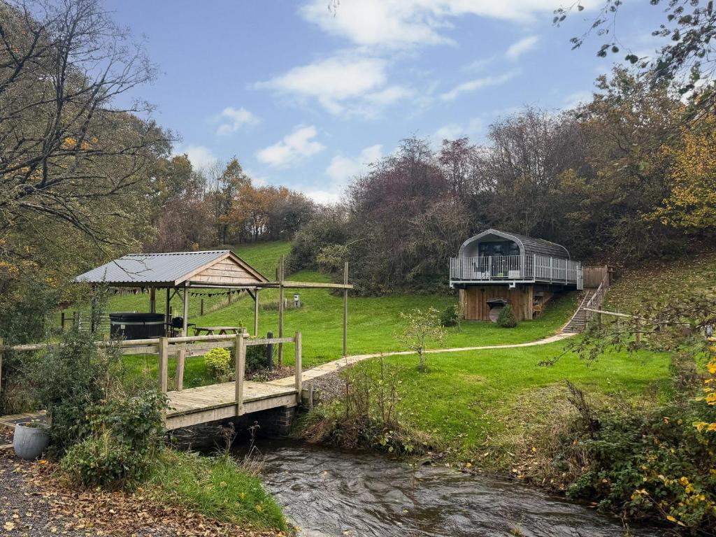 eine Holzbrücke über einen Fluss mit einem Haus im Hintergrund in der Unterkunft 1 Bed in Church Stretton 90929 in All Stretton