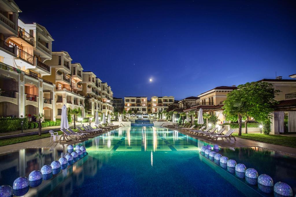 a hotel swimming pool with chairs and buildings at night at Green Life Apartments Sozopol in Sozopol