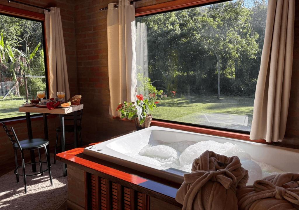 een badkuip in een kamer met een groot raam bij Refúgio com Hidro, Lareira, Café da Manhã e Vista da Natureza in Santo Antônio do Pinhal