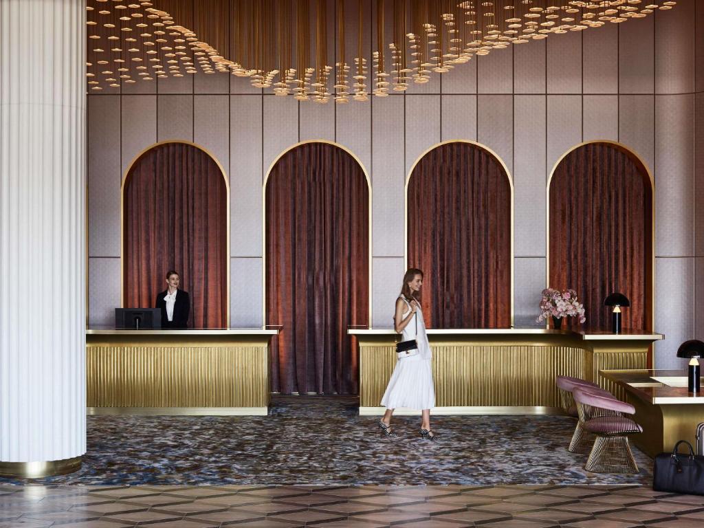 Una mujer caminando en el vestíbulo de un hotel con un mostrador de recepción. en Hotel Chadstone Melbourne MGallery Collection, en Chadstone
