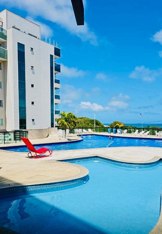 a swimming pool with a red chair in front of a building at Resort Praia Grande in Arraial do Cabo