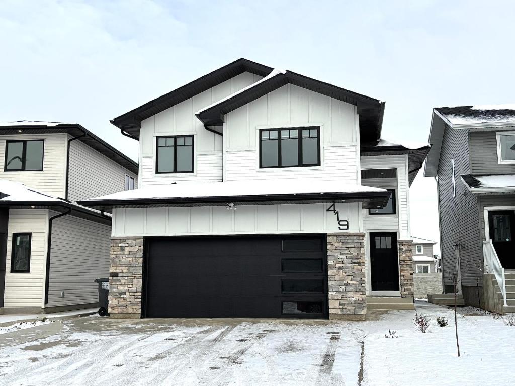 a white house with a garage in the snow at Cozy Heaven in Saskatoon