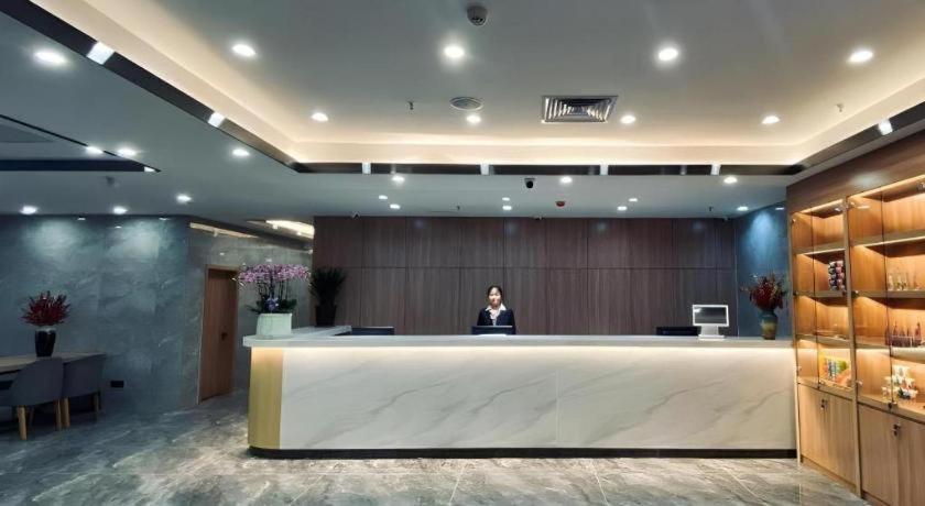 济南Shell Hotel Shandong Jinan Daming Lake的一名妇女在大厅的柜台后面站着