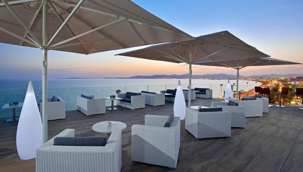 un patio con sillas blancas, mesas y sombrillas en Hotel Hispania en Playa de Palma