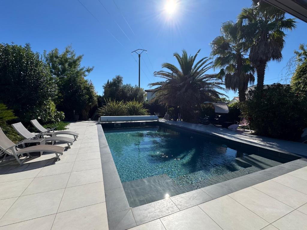una piscina in un cortile con sedie e alberi di Chez Isa - avec jacuzzi intérieur et piscine chauffée a Gigean