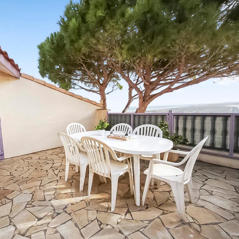 a white table and chairs on a patio with a tree at Appartement confortable avec parking et terrasse in Leucate-Plage