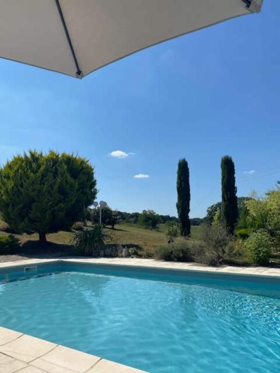 a swimming pool in a yard with an umbrella at Chez Gargatte, gîte 4 chambres, 12personnes , piscine privée chauffée de mai à septembre , FR in Ronsenac