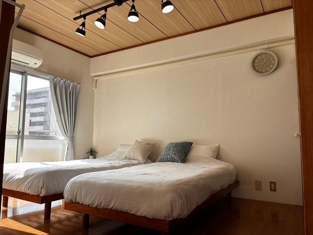 two beds in a room with a clock on the wall at Kumamoto Serviced Apartment Sakura Mee 桜美 in Kumamoto