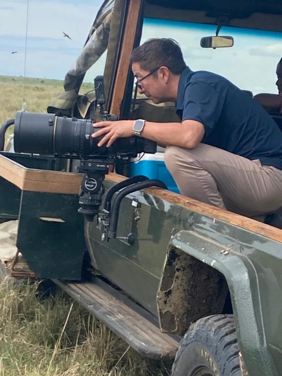 een man die met een camera achterin een militair voertuig zit bij Humble Resort in Masai Mara