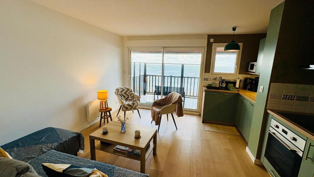 a living room with a couch and a table and a kitchen at Le Panorama, confortable appartement - accès direct à la plage in Bernières-sur-Mer