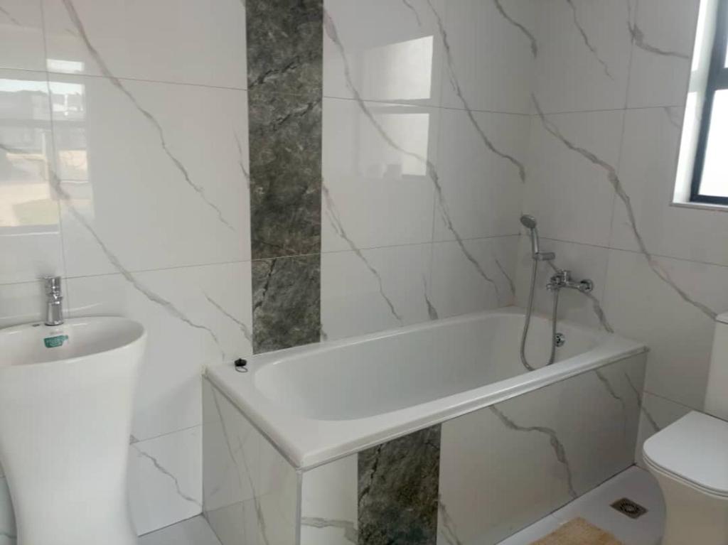 un bagno bianco con vasca e lavandino di Longhorn Ibex Apartments a Lusaka