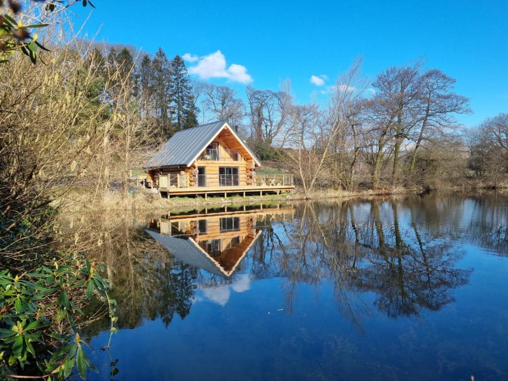 eine Blockhütte auf einem See mit Reflexion im Wasser in der Unterkunft Kingfisher Cabin in Broughton in Furness