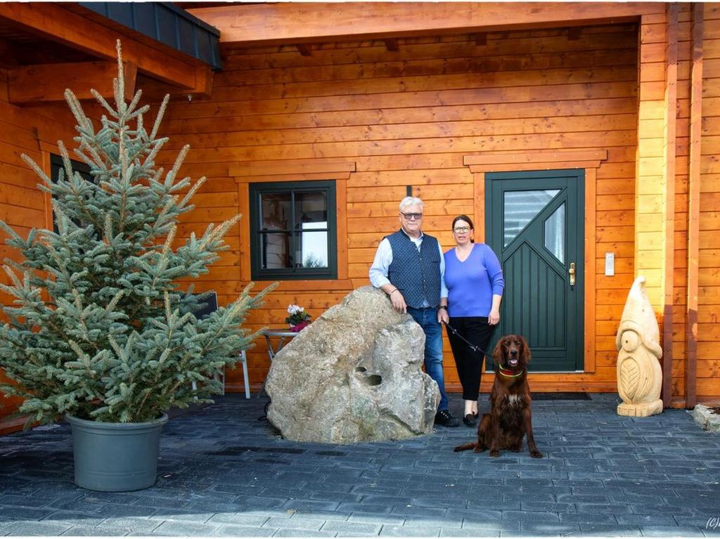 Un uomo e una donna in piedi davanti a una casa con un cane di Ferienwohnung Sußebach mit 80 Qm a Vöhringen