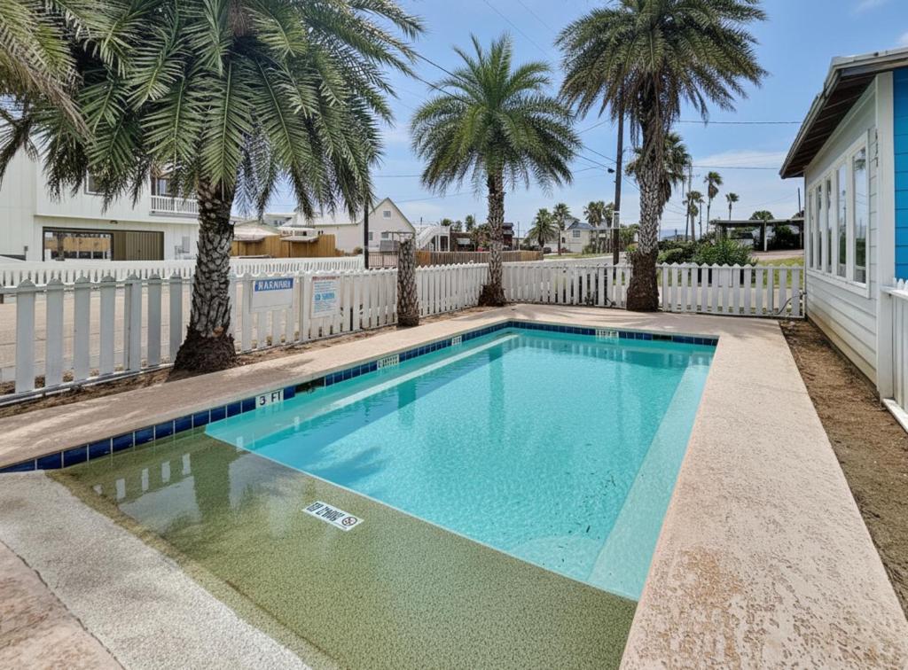 a swimming pool with palm trees and a white fence at Beach Club 1 in Port Aransas