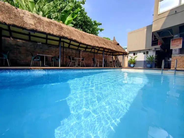 une grande piscine bleue avec un toit de chaume dans l'établissement AOTEL HOTEL Ikeja, à Ikeja