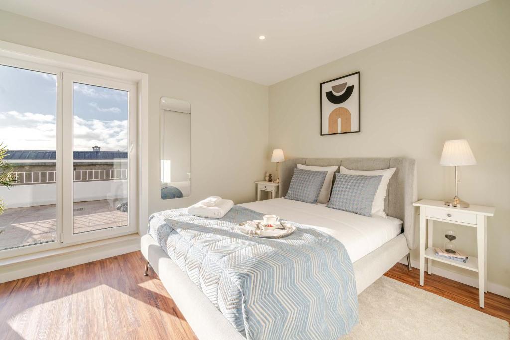 a white bedroom with a bed and a large window at Bright Beachside Flat with Terrace by HostWise in Matosinhos