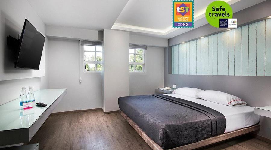 A modern double room with one bed, a wall-mounted television, and a built-in console.