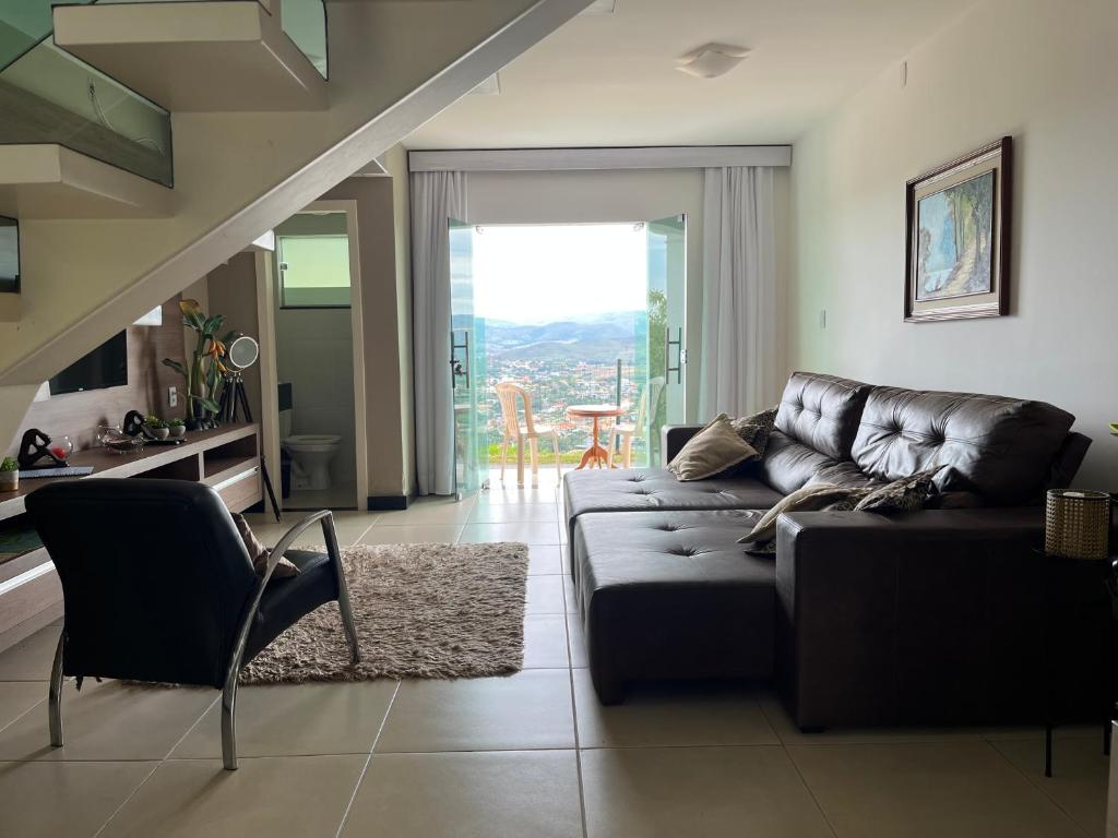 a living room with a leather couch and a staircase at Refúgio Escarpas do Lago Mirante 1702 in Capitólio