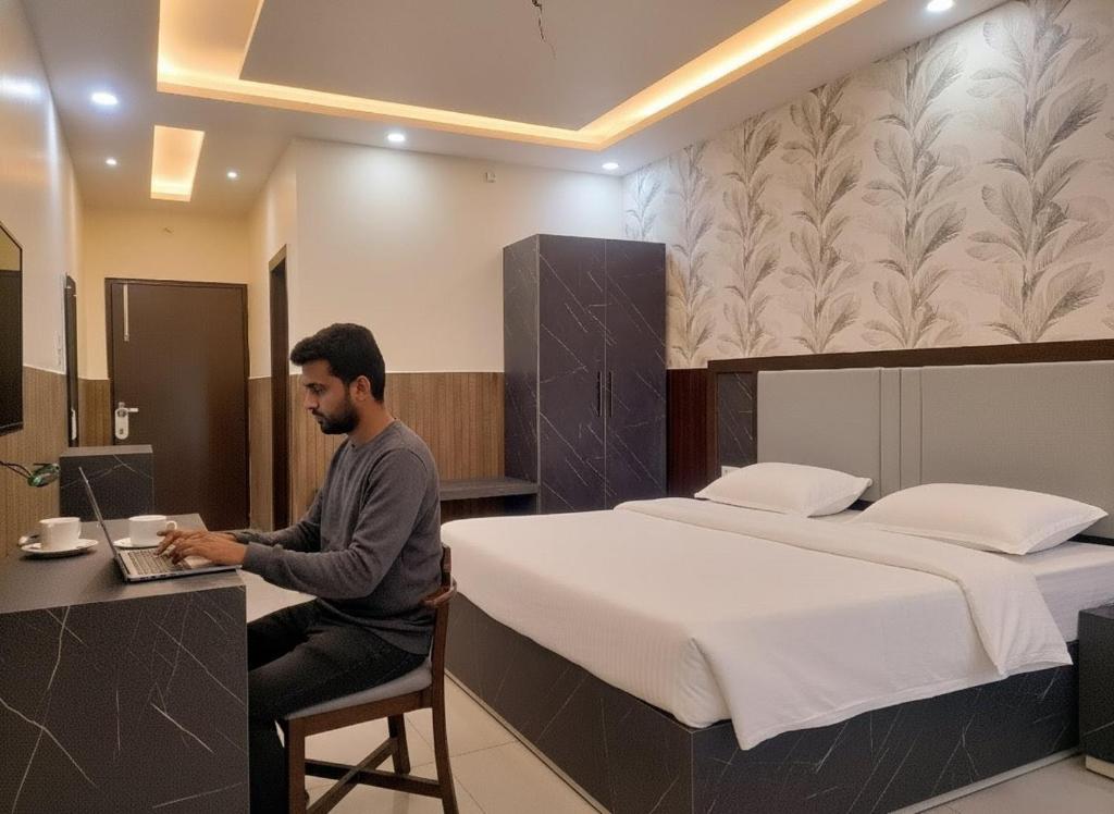 a man sitting at a desk in front of a bed at Cottage Club Inn in Almora