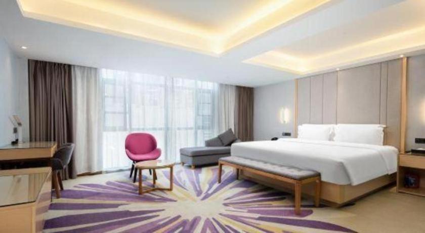 um quarto com uma cama grande e uma cadeira rosa em Lavande Hotel·Wuhan Qingshan Zhongyuan Plaza em Wuhan