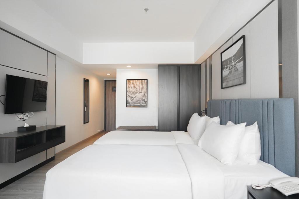 A bedroom with a wide white bed faces a wall-mounted television and built-in storage.
