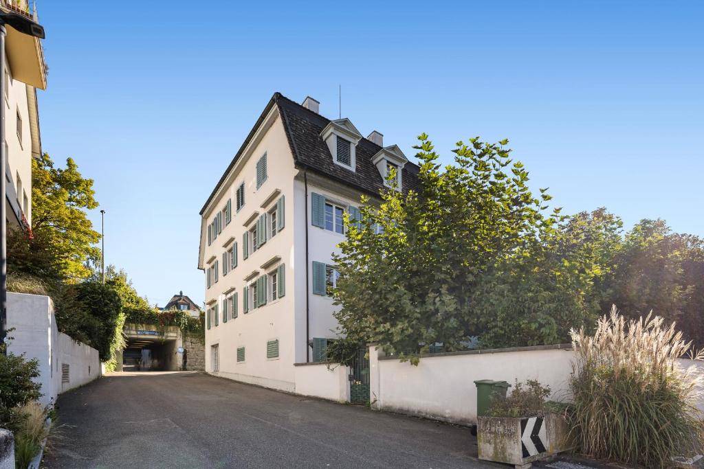 a white building with a black roof on a street at Spacious light-flooded apartment with garden at Lake Zurich in Männedorf