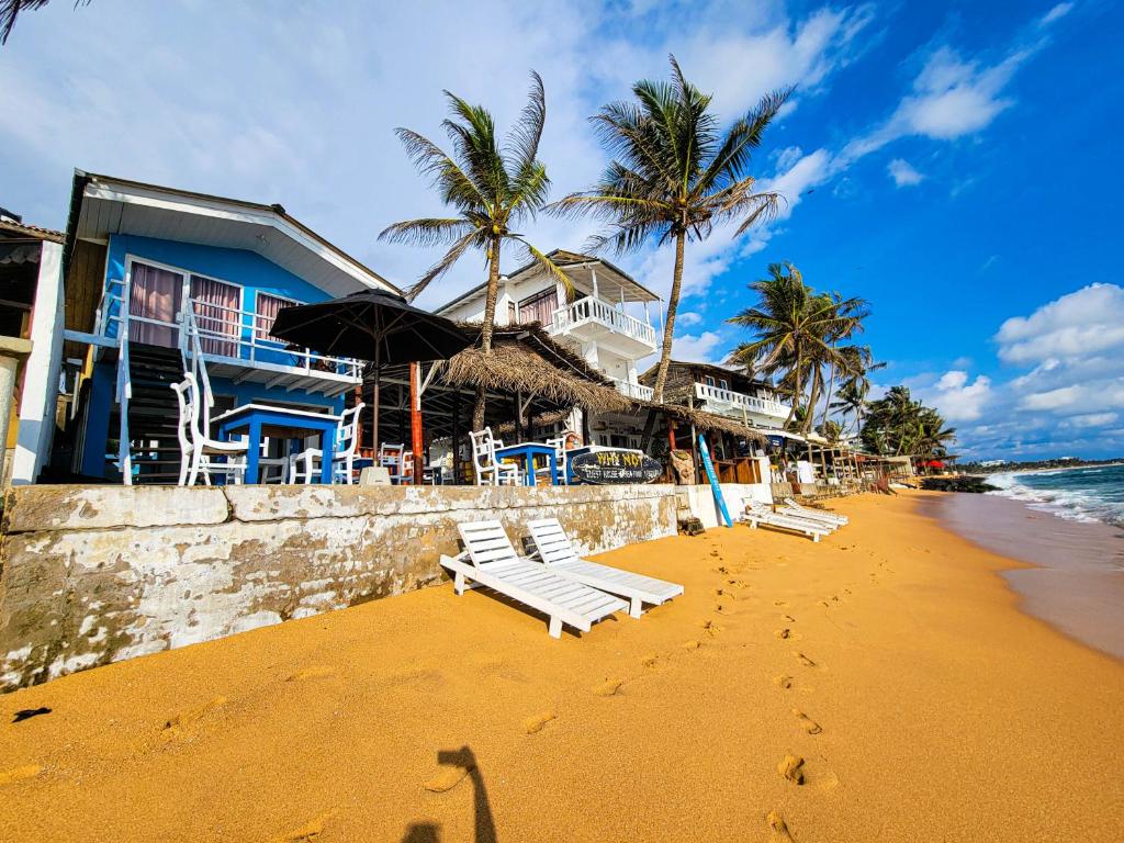 ein Strand mit weißen Bänken und Palmen und ein Gebäude in der Unterkunft Beach Cabana By why not hikkaduwa in Hikkaduwa