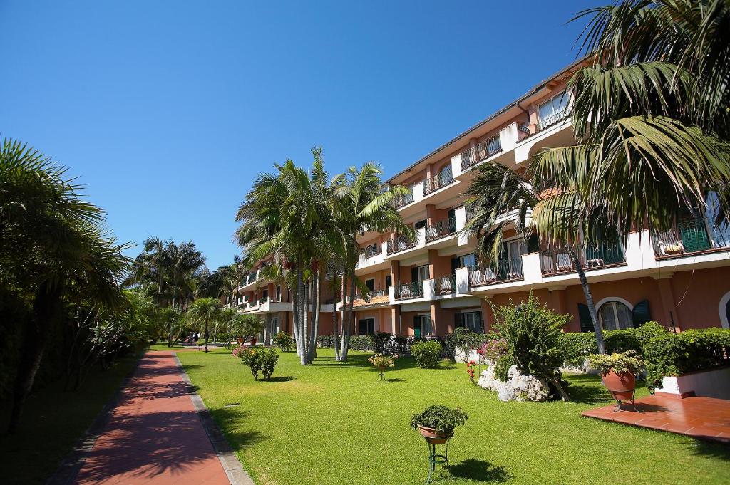 a large apartment building with palm trees and a lawn at Hotel Caparena in Taormina