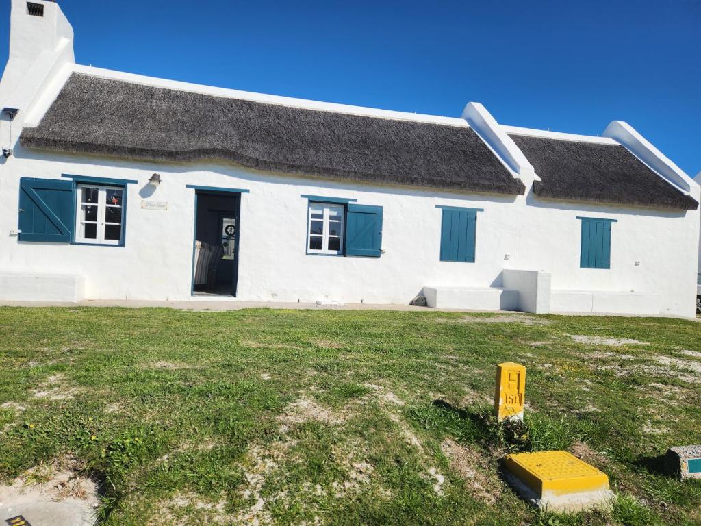 a white building with blue windows and a yard at Hannah's Close in Struisbaai